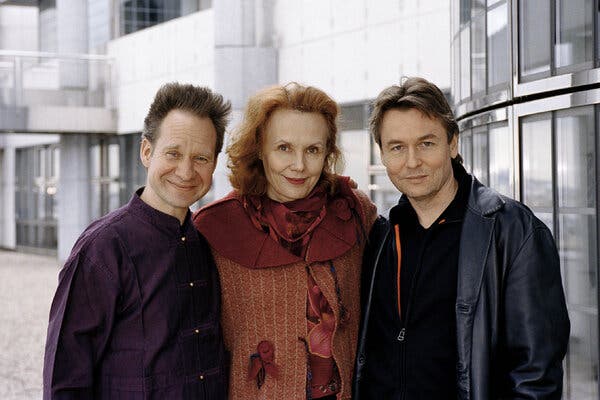 Peter Sellars, Ms. Saariaho and Esa-Pekka Salonen stand close together, smiling, in front of a building.