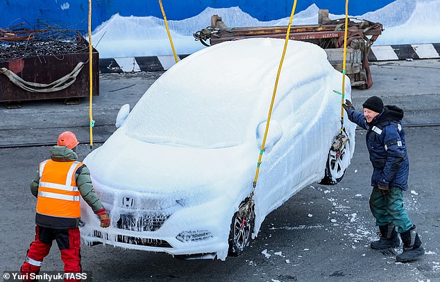 Two workers unload an ice-covered vehicle from the ship carrying cars from Japan in temperatures of -19C (-2F) in Russia's Pacific capital