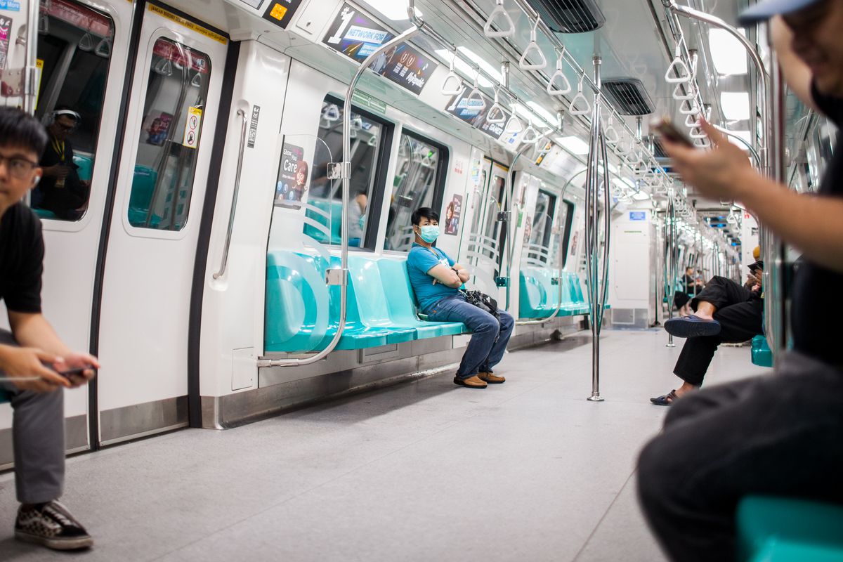 Residents, many in masks, sit several seats apart on a brightly lit train. 