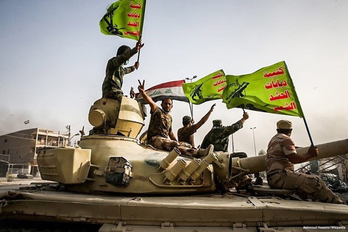 Image of militants raising the Iraq and Popular Mobilisation Forces (PMF) flag [Mahmoud Hosseini/Wikipedia]