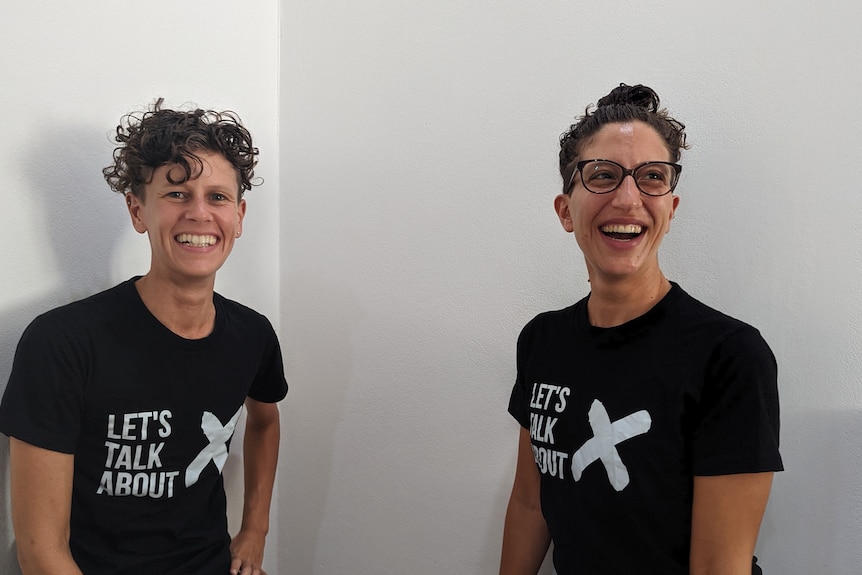 Two people with short dark hair smiling. They are both wearing dark T-shirts that says Let's Talk About X.