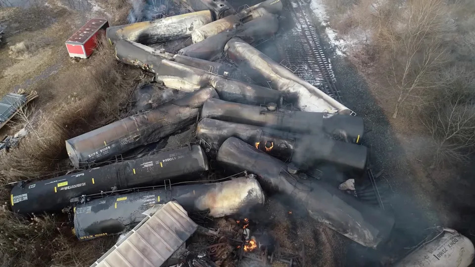An aerial shot shows about a dozen rail cars, packed together and still smoking, after the derailment.