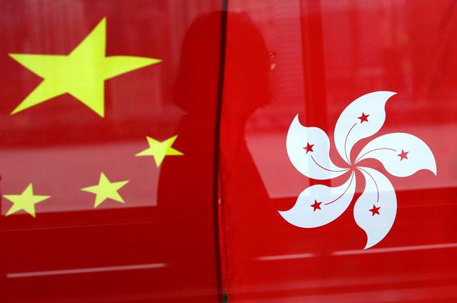 FILE PHOTO - A woman is reflected in a window behind Chinese and Hong Kong flags after celebrations commemorating the 20th anniversary of Hong Kong's handover to Chinese sovereignty from British rule, in Hong Kong, China July 2, 2017. REUTERS/Tyrone SiuTyrone Siu