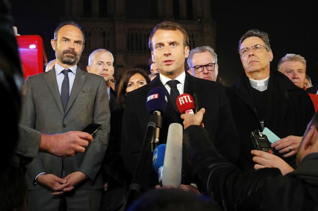 French President Emmanuel Macron speaks as Prime Minister Edouard Philippe and Archbishop of Paris, Michel Aupetit, stand near the Notre Dame Cathedral where a fire burns in Paris, France, April 15, 2019.   REUTERS/Philippe Wojazer/Pool