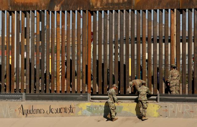 FILE PHOTO: U.S. soldiers walk next to the border fence between Mexico and the United States, as migrants are seen walking behind the fence, after crossing illegally into the U.S. to turn themselves in, in El Paso, Texas, U.S., in this picture taken from Ciudad Juarez, Mexico, April 3, 2019. The writing on the wall reads, Help us Jesus Christ. REUTERS/Jose Luis Gonzalez/File Photo