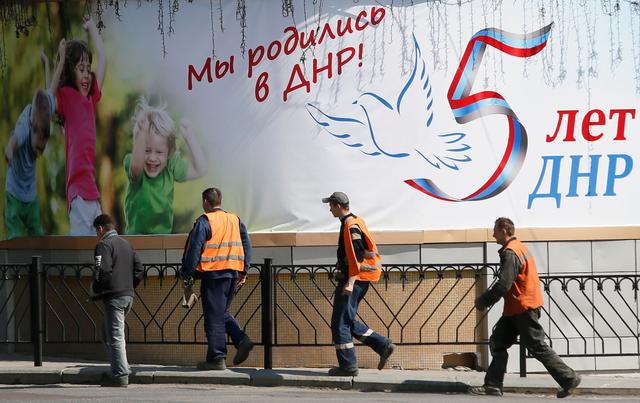 Men walk past a banner, which reads We were born in DPR (Donetsk People's Republic)! DPR is five years old, in a street in the separatist-controlled city of Donetsk, Ukraine April 25, 2019. REUTERS/Alexander Ermochenko