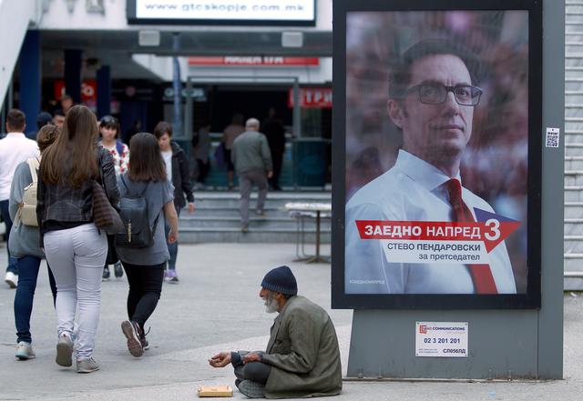 A man begs for coins next to an election campaign poster of the ruling Social Democratic Union (SDSM) candidate Stevo Pendarovski before the presidential election on May 5 in Skopje, North Macedonia May 4, 2019. REUTERS/Ognen Teofilovski