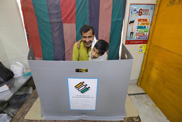 A man holding a child reacts behind a voting compartment as he prepares to cast his vote at a polling station during the sixth phase of the general election, in New Delhi, India, May 12, 2019. REUTERS/Anushree Fadnavis