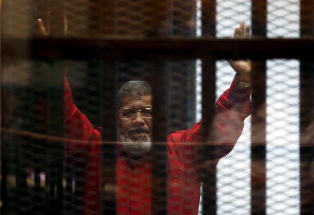 FILE PHOTO: Egypt's deposed president Mohamed Mursi greets his lawyers and people from behind bars at a court wearing the red uniform of a prisoner sentenced to death, during his court appearance with Muslim Brotherhood members on the outskirts of Cairo, Egypt, June 21, 2015. REUTERS/Amr Abdallah Dalsh/File Photo