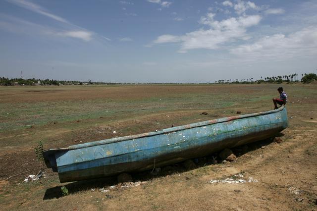 A man sits on a fishing boat stranded on the bed of dried-up lake in Thiruninravur, India, June 29, 2019. Picture taken June 29, 2019. REUTERS/P. Ravikumar