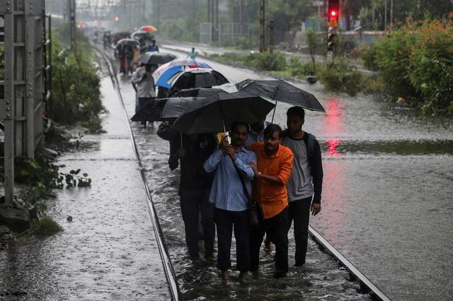 Commuters walk on waterlogged railway tracks after getting off a stalled train during heavy monsoon rains in Mumbai, India, July 2, 2019. REUTERS/Francis Mascarenhas