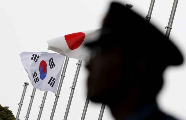 FILE PHOTO: A police officer stands guard near Japan and South Korea national flags at a hotel, where the South Korean embassy in Japan is holding the reception to mark the 50th anniversary of the normalisation of ties between Seoul and Tokyo, in Tokyo  June 22, 2015.   REUTERS/Toru Hanai/File Photo