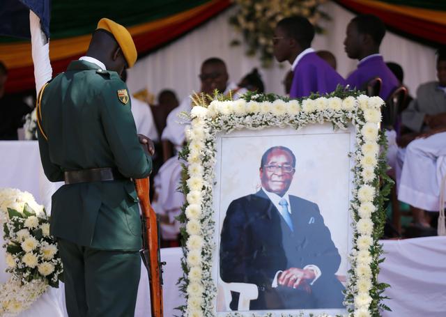 A soldier stands beside a picture of former Zimbabwean President Robert Mugabe during a church service at his rural village in Kutama, Zimbabwe, September 28, 2019. REUTERS/Philimon Bulawayo