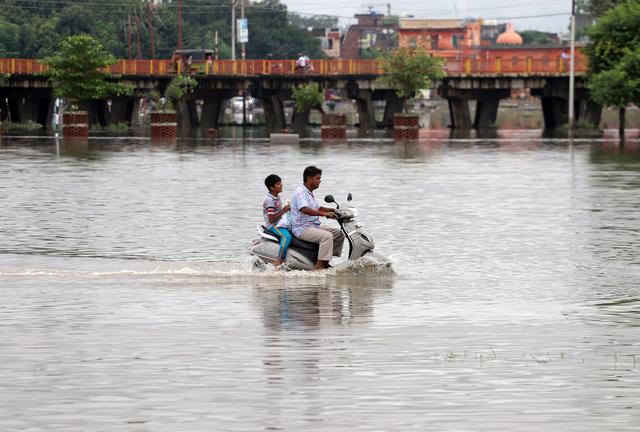 A man and a boy ride a scooter through a flooded road after heavy rains in Prayagraj, India, September 29, 2019. REUTERS/Jitendra Prakash