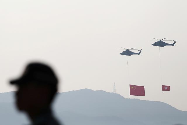 A police officer stands guard as helicopters carrying China's national flag and Hong Kong's flag fly past, on China's National Day at Tsim Sha Tsui in Hong Kong, China October 1, 2019. REUTERS/Athit Perawongmetha