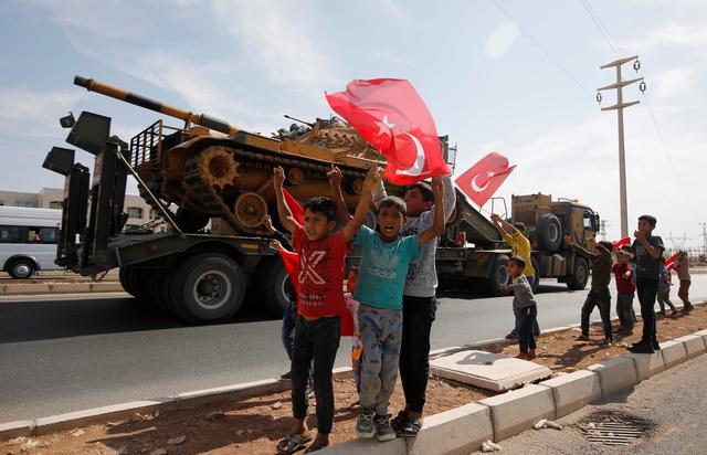 Boys wave Turkish flags as a military convoy drives near the border town of Akcakale in Sanliurfa province, Turkey, October 14, 2019. REUTERS/Kemal Aslan 