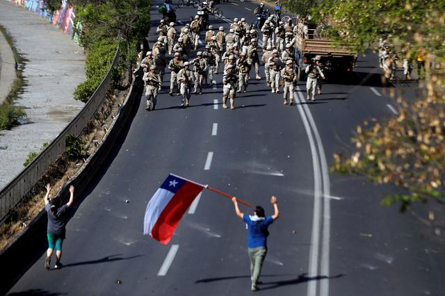 FILE PHOTO: Chilean soldiers gather near demonstrators, one of whom holds a Chilean flag, during a protest against Chile's state economic model in Santiago, Chile, October 20, 2019. REUTERS/Edgard Garrido/File Photo