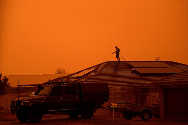 A resident uses a garden hose to wet down the house as high winds push smoke and ash from the Currowan Fire towards Nowra, New South Wales, Australia January 4, 2020. REUTERS/Tracey Nearmy