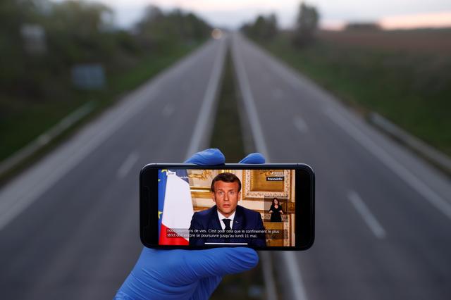 A mobile phone showing French President Emmanuel Macron, as he addresses the nation about the coronavirus disease (COVID-19) outbreak, is displayed for a photo in front of an almost empty motorway in Strasbourg, France, April 13, 2020. REUTERS/Christian Hartmann