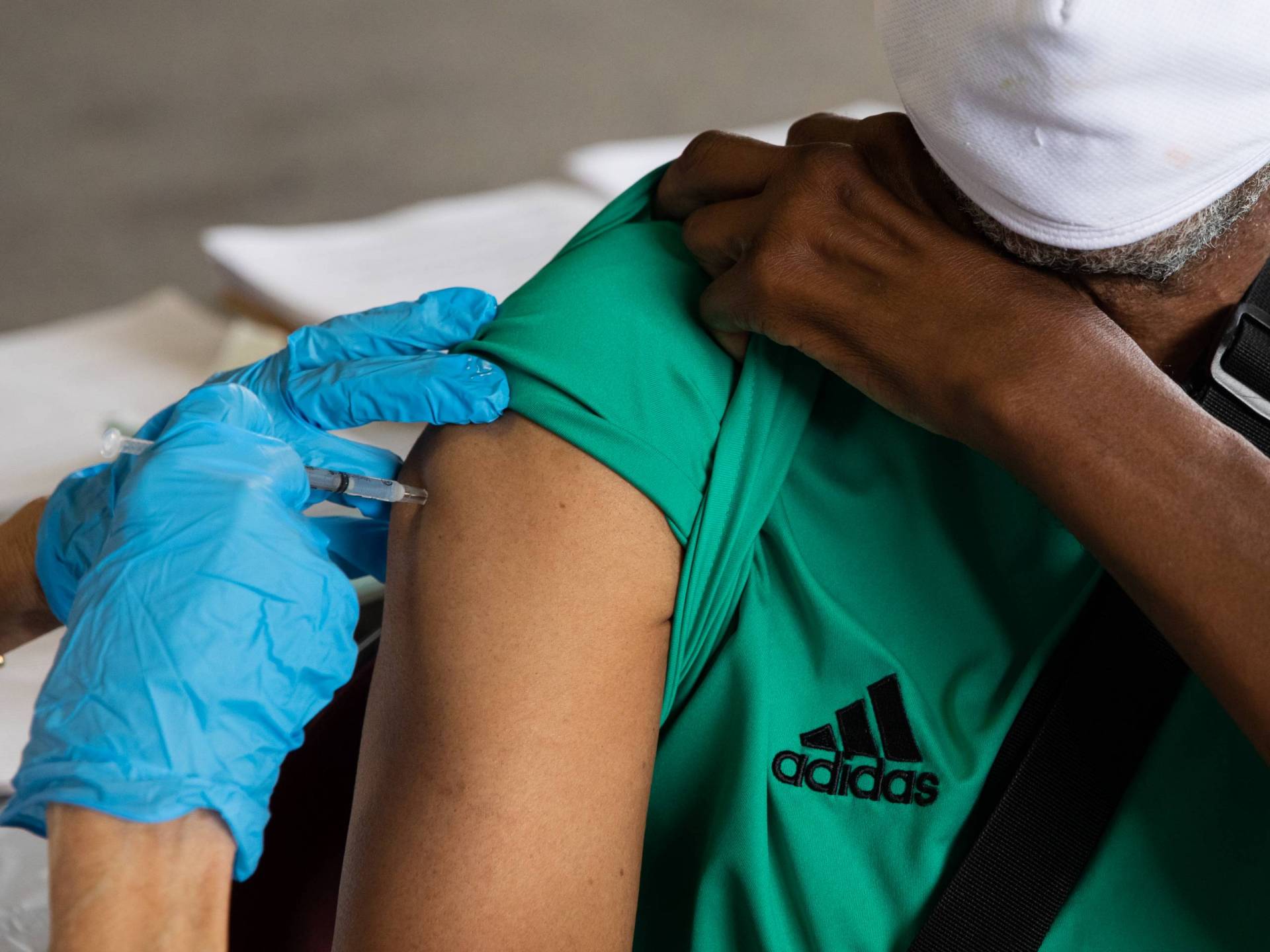 Blue-gloved hands administer a vaccine into a shoulder. Blue-gloved hands administer a vaccine into a shoulder.